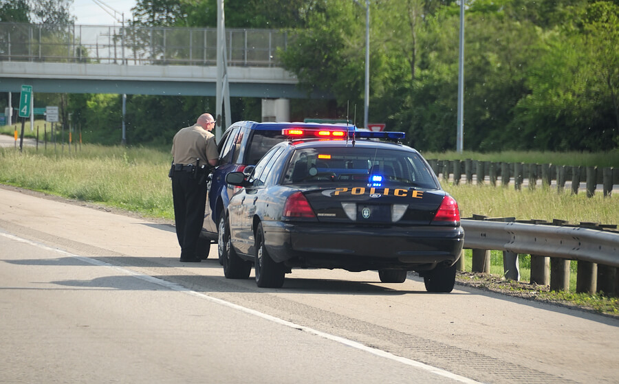 A police cruiser with the lights flashing has stopped a speeding car along the interstate highway and is issuing a ticket.